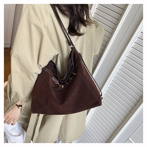 Dettaglio di una borsa a spalla in pelle scamosciata marrone indossata da una modella
