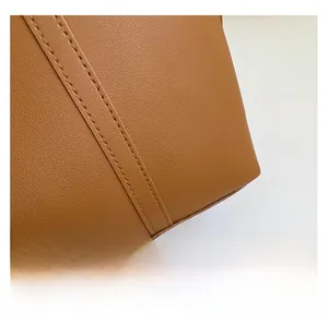 Macro detail of brown lychee grain leather texture and precise double stitching of tote bag