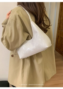Dettaglio della borsa hobo bianca con texture a serpente e logo del marchio sul cappotto