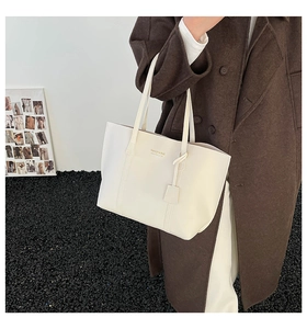 Detailed close-up of cream-white leather tote bag with FASHION & BAG print and charm