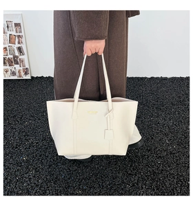 Detailed close-up of a white leather tote bag with gold logo and elegant charm