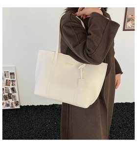 Detailed side view of white faux leather tote bag with gold lettering and shoulder strap