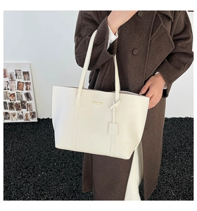 Close-up of a white leather tote bag with gold lettering and a matching hanging tag accessory