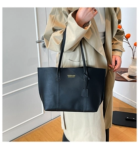 Detail of a black matte leather tote bag with gold lettering shown on a model's shoulder
