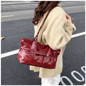 Detailed close-up of dark red glossy tote bag with stylish buckles on street background