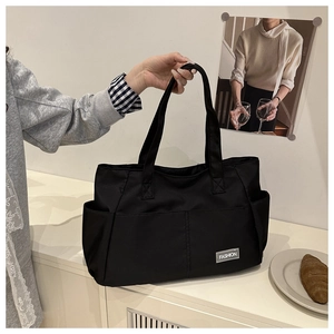 Dettaglio borsa tote nera che mostra la tasca laterale e l'etichetta moda bianca