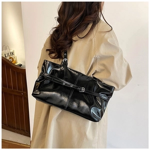 Détail d'un sac cabas noir brillant avec boucle argentée porté sur un trench-coat beige
