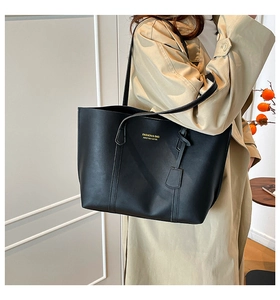 Détail d'un sac cabas en cuir noir avec lettrage doré et un pendentif en cuir élégant