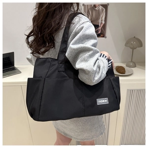 Dettaglio della borsa tote in nylon nero con etichetta fashion e tasca laterale sul modello