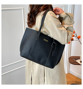 Model wearing a black faux leather tote bag with gold lettering and decorative stitching
