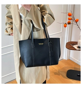 Detail view of large black tote bag with white contrast stitching on beige trench coat