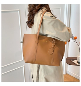 Close-up of brown leather tote bag with gold lettering and decorative pendant detail