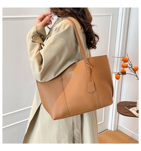 Close-up of caramel faux leather tote bag with gold lettering and charm accessory