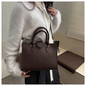 Dettaglio di una borsa in pelle marrone scuro con finiture dorate indossata da una modella