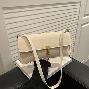 Borsa sottospalla beige minimalista con fibbia in metallo dorato su sfondo libro