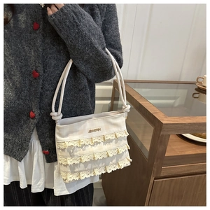 Dettaglio della borsa tote in pizzo crema con balze a tre strati e logo in metallo