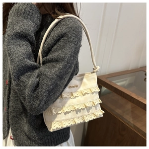Dettaglio delle balze in pizzo crema e del logo dorato su una borsa tote da donna