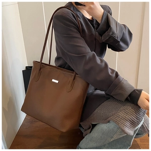 Dettaglio di grande borsa tote marrone con texture a grana e placca logo argento