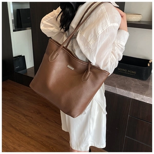 Dettaglio di una grande borsa tote in pelle martellata marrone scuro portata a spalla