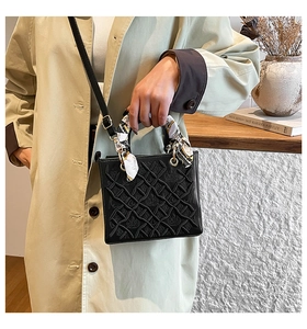 Dettaglio borsa nera con trama a rilievo, manico avvolto da foulard in seta e tracolla sottile