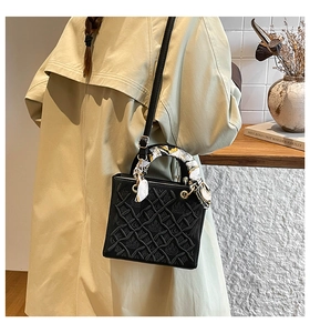 Dettaglio borsa a tracolla in pelle nera trapuntata con foulard decorativo e finiture dorate