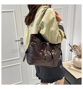Dettaglio di una grande borsa tote marrone con fiocchi a rilievo, indossata dalla modella
