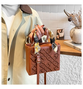 Dettaglio della borsa in pelle marrone con trama goffrata e manico con foulard di seta