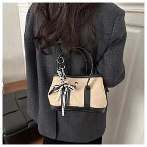 Dettaglio borsa scamosciata beige con finiture nere e ciondolo fiocco in pizzo nero e bianco