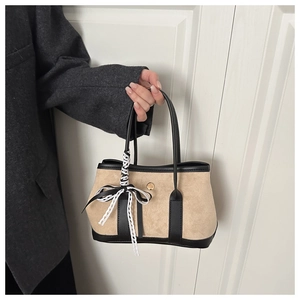 Dettaglio borsa tote beige con cinturini neri, chiusura dorata e ciondolo a fiocco