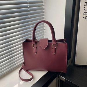 Elegante borsa tote in pelle bordeaux con finiture dorate e manici su un davanzale