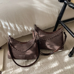 Borsa a mezzaluna in camoscio marrone scuro con catena in metallo e tracolla su letto