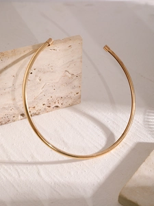 Dettaglio macro di un choker rigido placcato oro minimalista su pietra strutturata