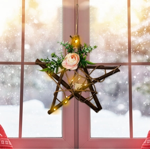 Star-shaped twig wreath with pink roses and LED lights hanging against a snowy window