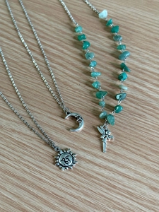 Detail of sun, moon, and green gravel stone pendant necklaces on wood texture
