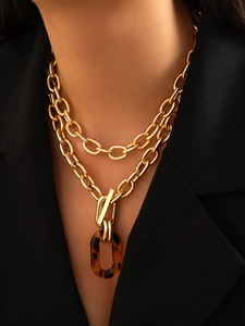 Détail d'un collier à double chaîne dorée avec fermoir OT et pendentif ovale ambré