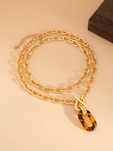 Détail d'un collier à grosse chaîne dorée avec fermoir OT et pendentif écaille de tortue
