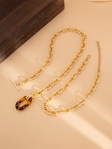 Détail du collier à grosse chaîne dorée avec pendentif en résine ambrée et fermoir T