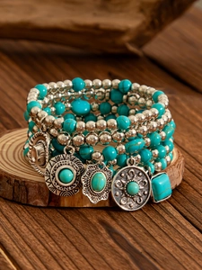 Detail of bohemian turquoise beaded bracelet set with silver charms on wooden base