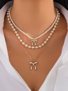 Dettaglio della collana a tre strati con perle bianche e ciondoli a fiocco moda