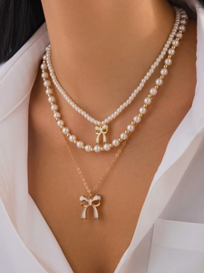 Dettaglio della collana a tre strati con perle bianche e ciondoli a fiocco dorati