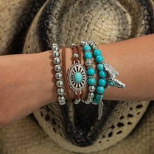Detail of bohemian layered bracelets with turquoise, silver feather and wolf head charms