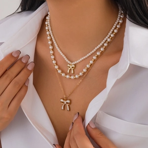 Collana a tre strati con fiocchi perle bianche e dettagli dorati su camicia bianca