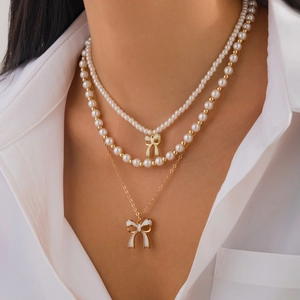Collana a tre strati con perle bianche e ciondoli a fiocco dorato indossata da una modella