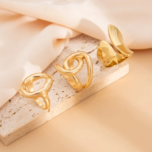 Macro detail of three polished gold geometric rings on a textured stone surface