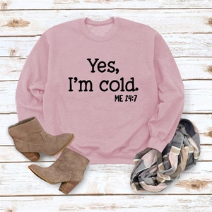 Pink sweatshirt detail with 'Yes I'm cold' print on wood background with winter boots