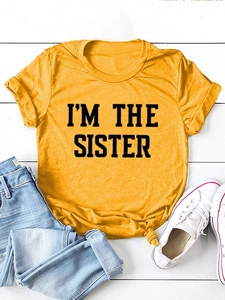 T-shirt jaune en coton avec imprimé I'M THE SISTER posé à plat sur fond bois blanc