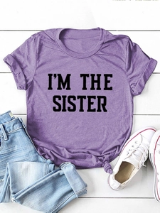 T-shirt violet 'I'M THE SISTER' avec ourlet noué et jean bleu posé à plat sur bois