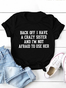 Flat lay of black crew neck T-shirt with white slogan print on a rustic wooden background