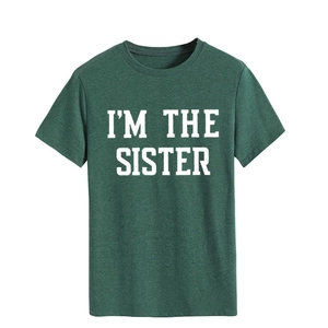 Gros plan du texte blanc 'I'M THE SISTER' imprimé sur un T-shirt en coton vert foncé
