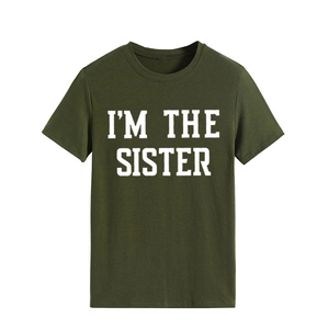 Gros plan de l'imprimé blanc « I'M THE SISTER » sur un t-shirt vert foncé à col rond